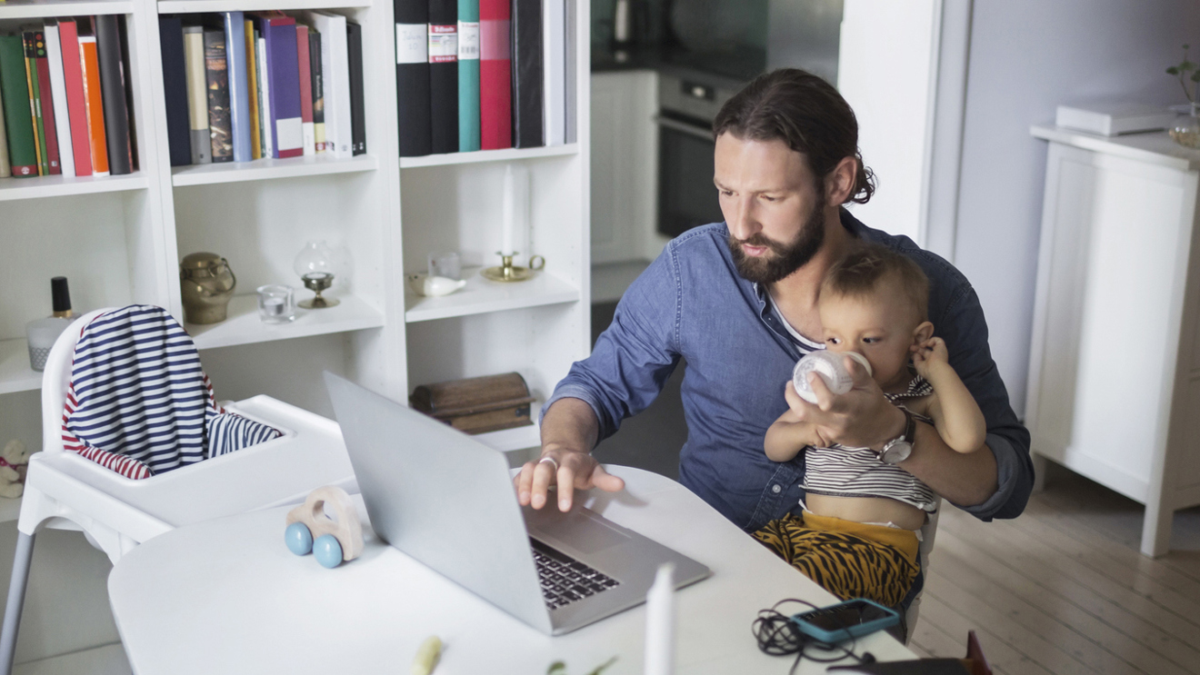 Pappa framför en dator med ett barn i famnen