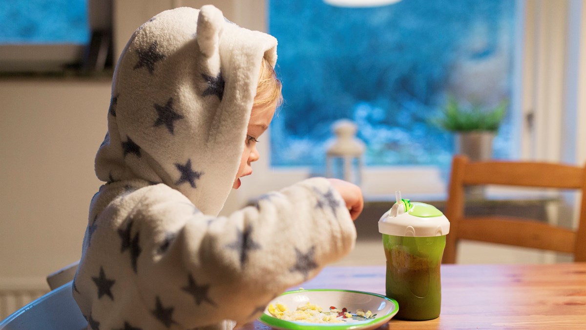 Ett barn iklädd morgonrock äter i gryning eller skymning