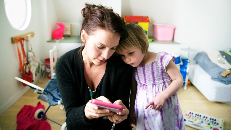 En kvinna och en flicka tittar i en mobiltelefon i ett barnrum.